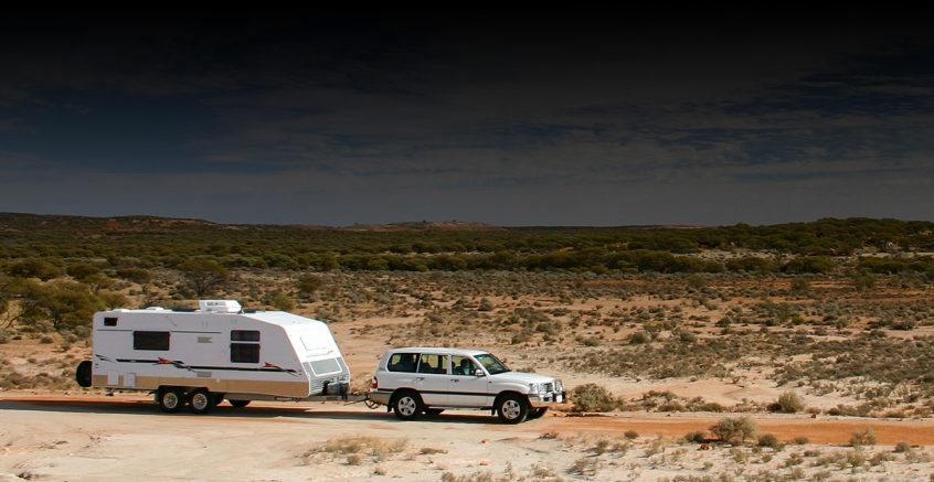 An SUV towing a large caravan is pictured in the arid outback of australia